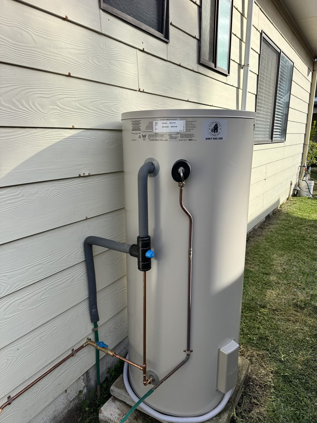 A new electric storage hot water system installed against the exterior wall of a weatherboard house