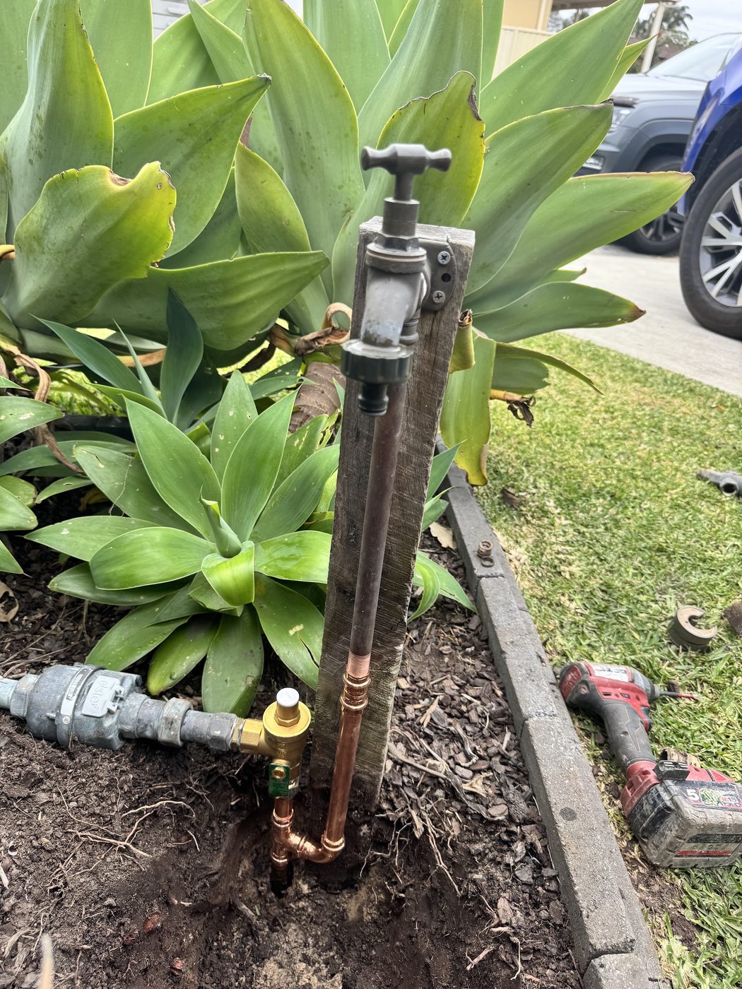 A new outdoor garden tap and copper pipe installation set into a garden bed, with tools beside the work