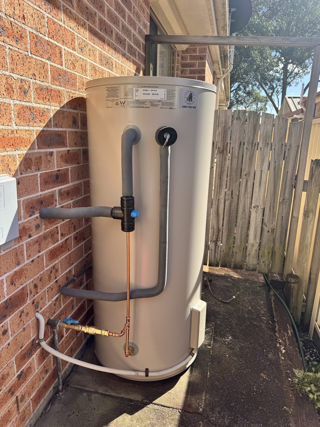 A replacement hot water system installed against a brick house exterior, with the Silverback Plumbing sticker on the tank