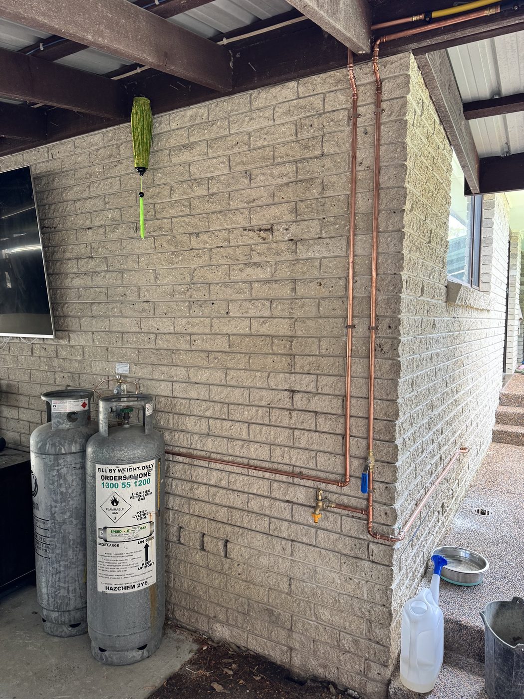 A copper gas line run neatly along an outdoor brick wall with two LPG cylinders connected